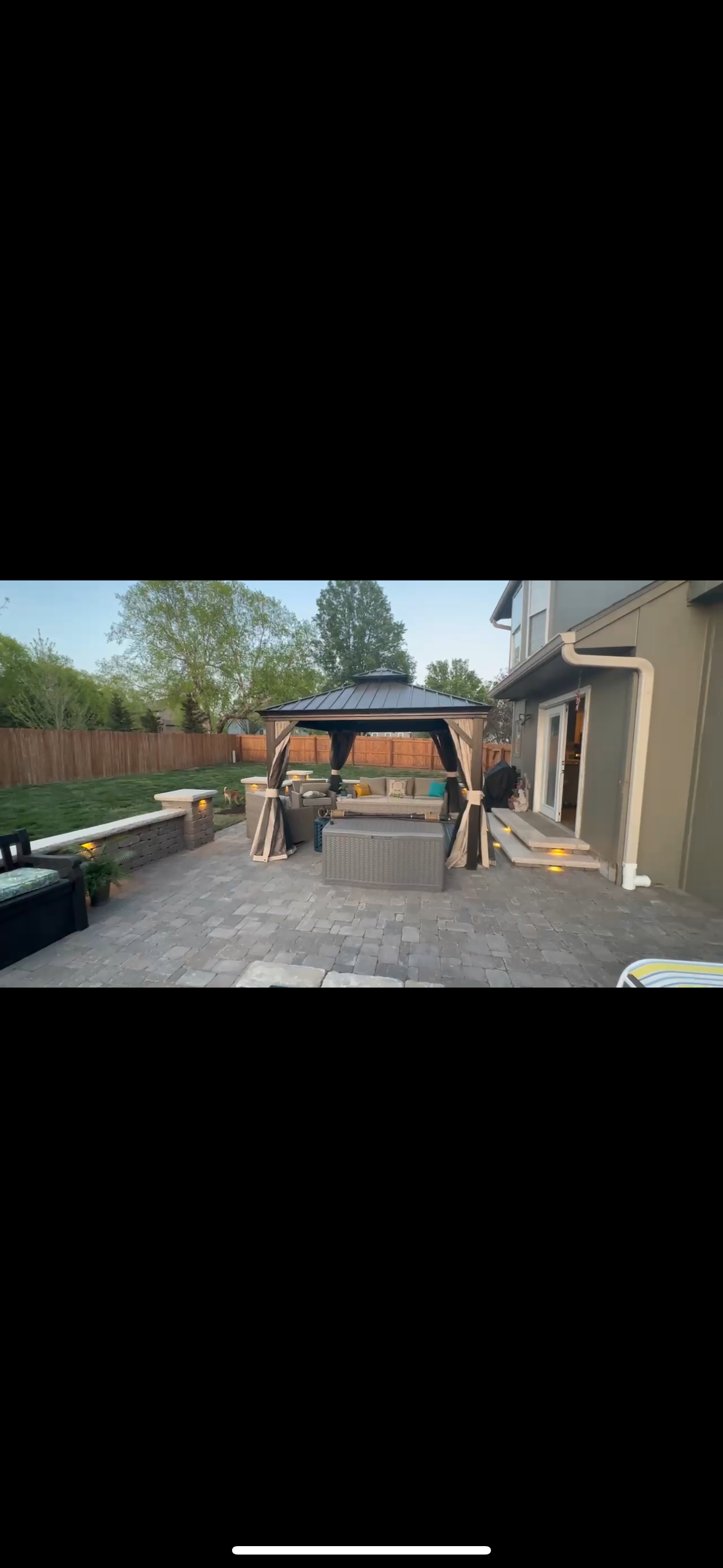 Backyard patio with gazebo, stone pavers, a low wall, and the house.