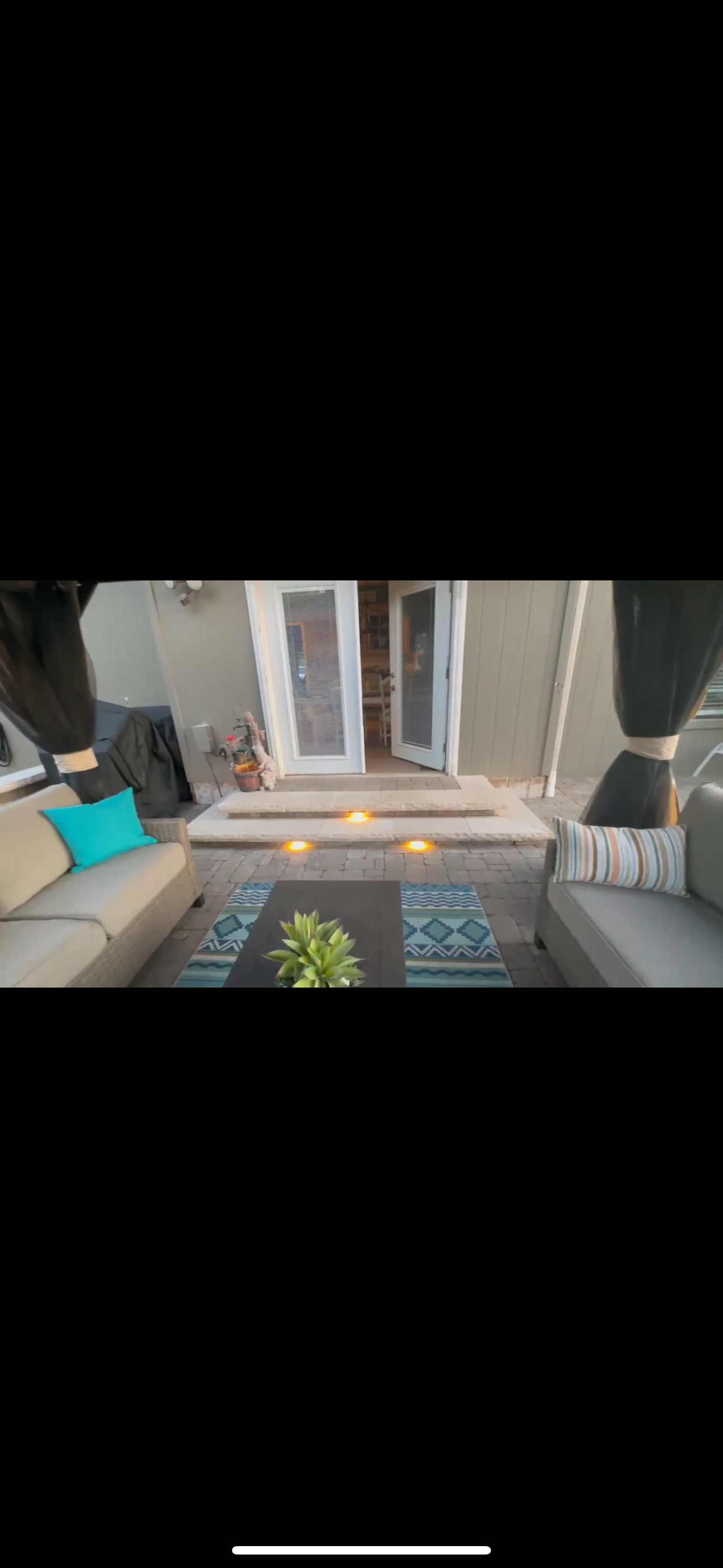 Outdoor seating area with couches, a fire pit, and a table with greenery, in front of a doorway.