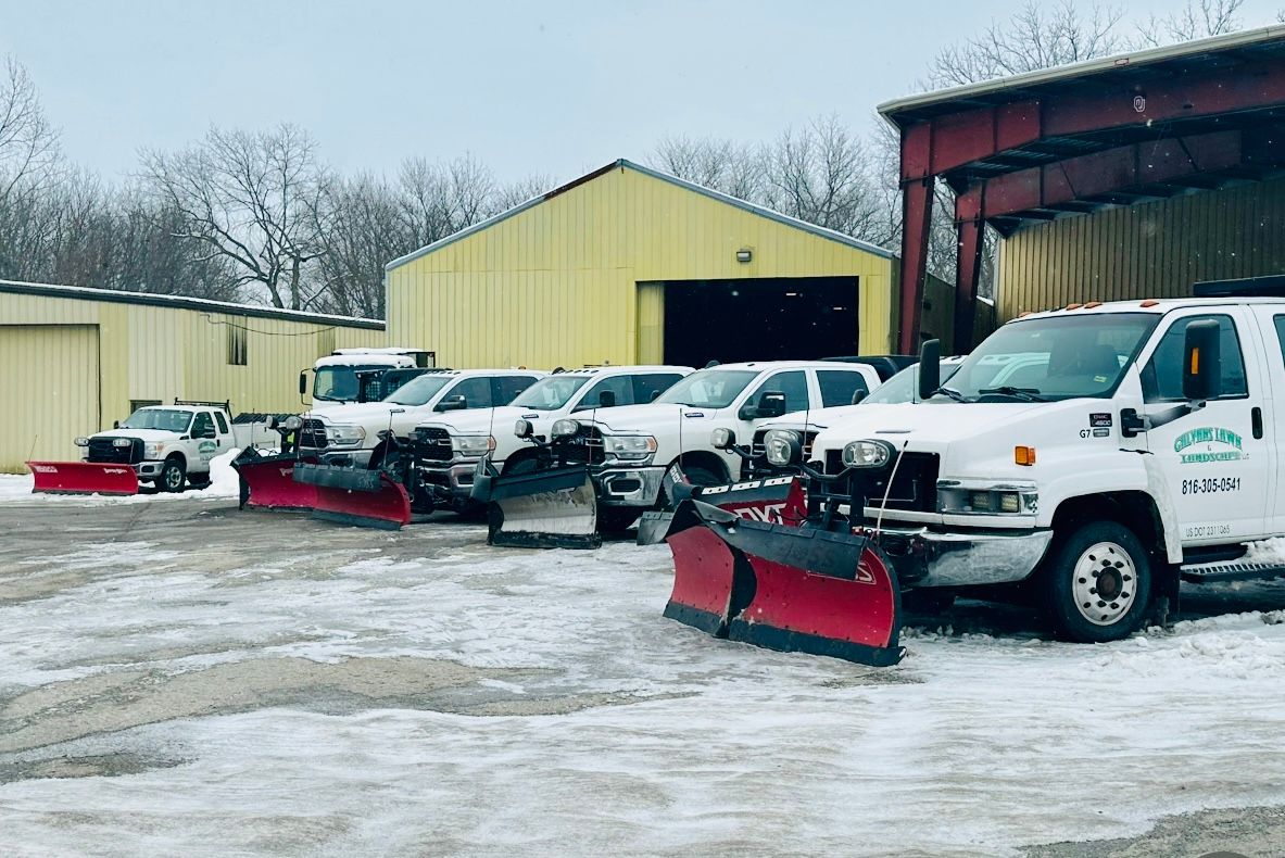 Snow plows parked in front of a yellow building on a snow-covered lot.