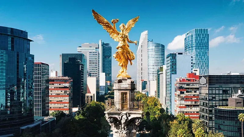 Estatua del Ángel Dorado de la Independencia sobre un monumento, rodeada de modernos rascacielos en la Ciudad de México.