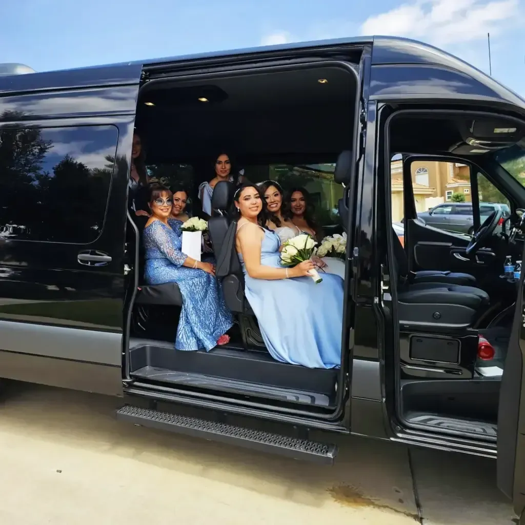 Damas de honor con vestidos de color azul claro posando en la puerta abierta de una camioneta de pasajeros negra.