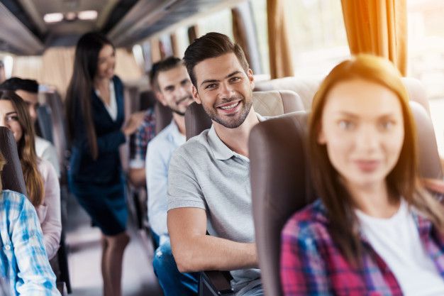 Personas en un autobús sonriendo a la cámara. Los pasajeros están sentados y una persona de pie en el pasillo.