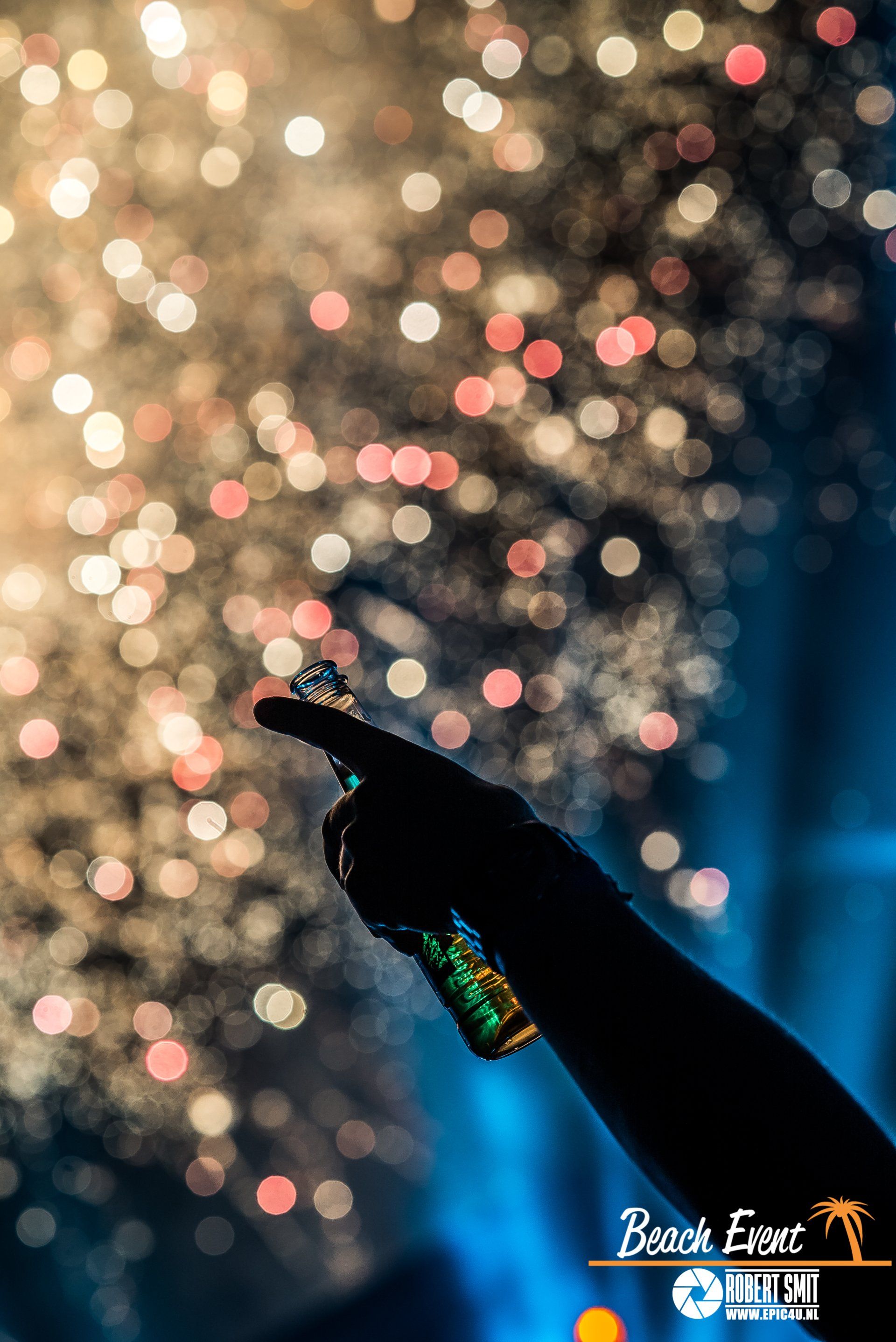 Silhouet van een arm die een bierfles vasthoudt, vuurwerk op de achtergrond. Logo van het strandevenement onderaan.