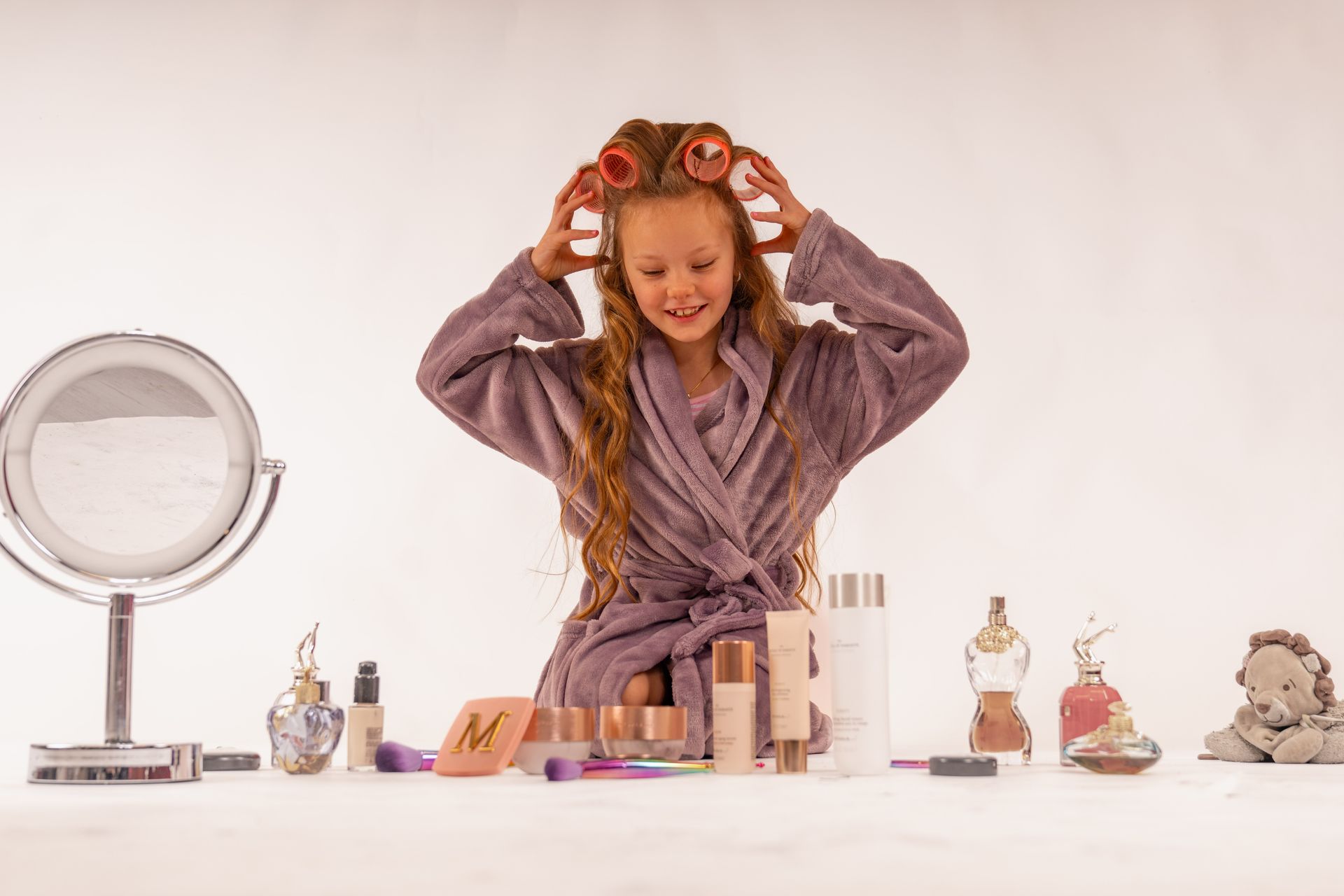 Meisje in een ochtendjas met haarkrulspelden, lachend naar de make-up op een tafel.