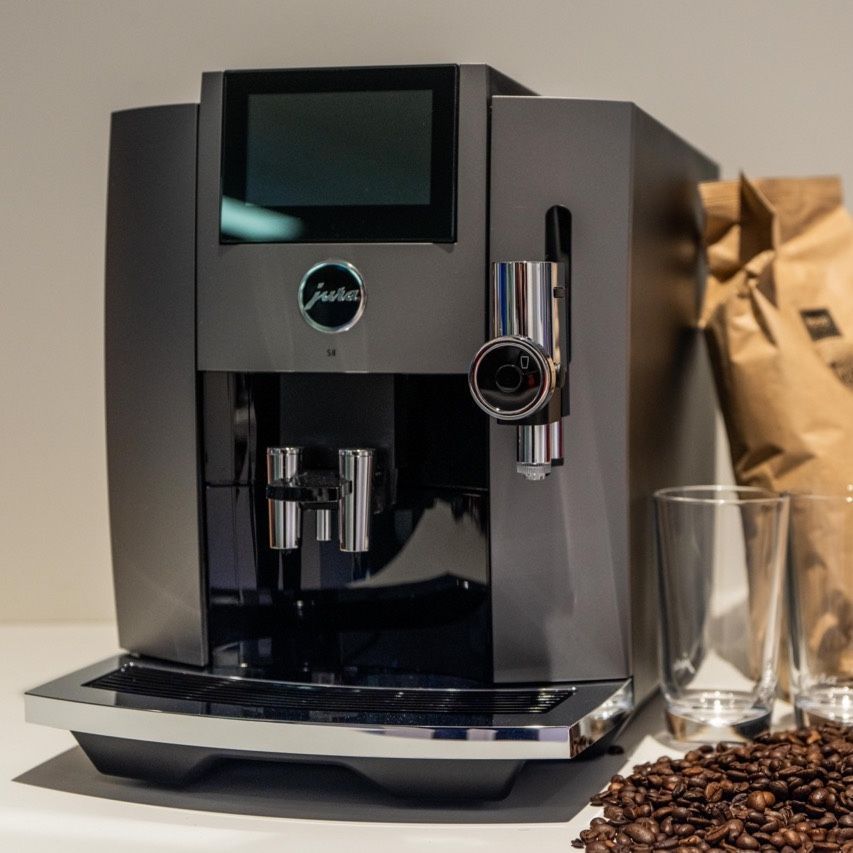 Donkergrijze Jura espressomachine met touchscreen, chromen accenten, koffiebonen en glazen.