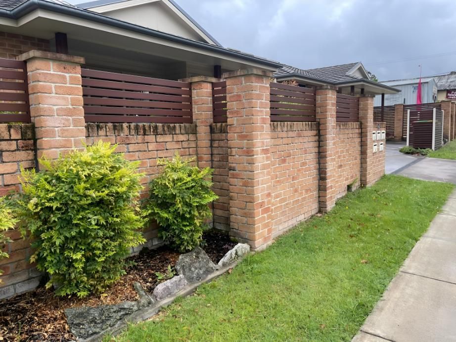 Brick front yard fence with trimmed shrubs beside a sidewalk and grassy strip — Hastings Services in Port Macquarie, NSW