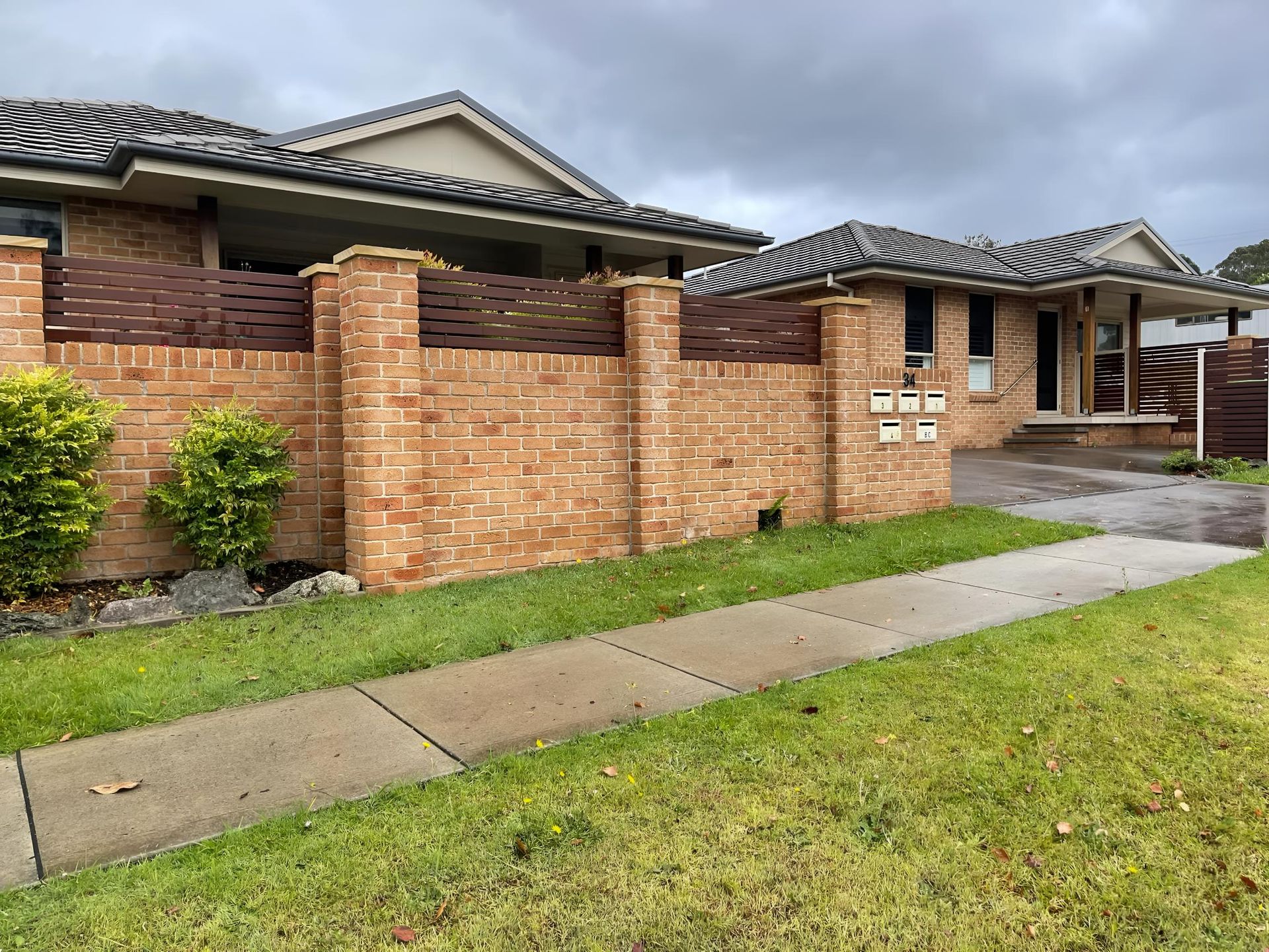 Brick house with a tiled roof, front yard, and wet sidewalk under a cloudy sky — Hastings Services in Port Macquarie, NSW