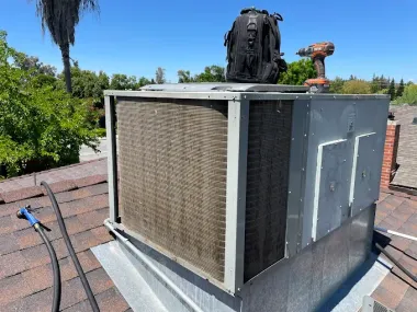 HVAC unit on a rooftop, with tools and a backpack. The unit has a metal frame and coils.