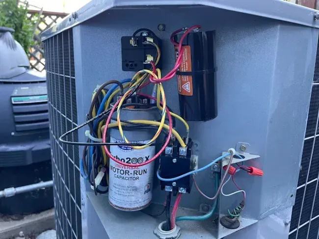 Air conditioner unit's electrical components: capacitor, contactor, wiring, in outdoor setting.