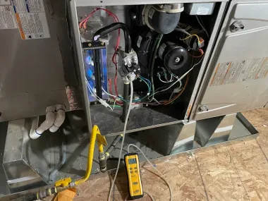 Furnace interior with a gas line and a yellow meter for testing. Wires and components are visible.