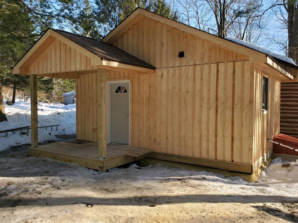 A small wooden house with a porch and a garage in the snow.