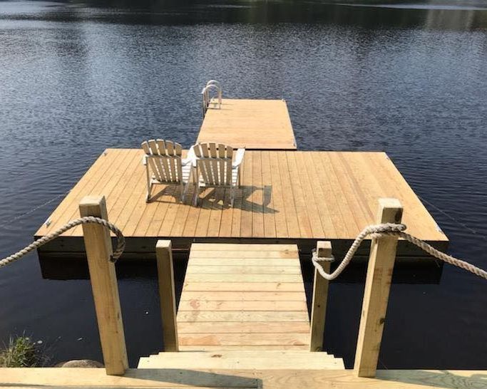 A wooden dock with two chairs on it in the middle of a lake.