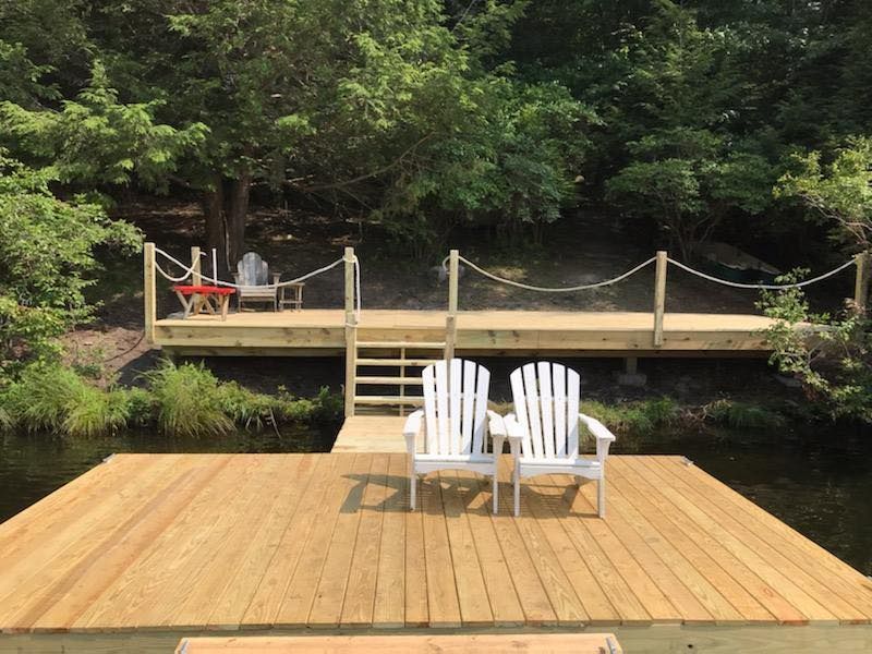 Two white adirondack chairs sit on a wooden dock