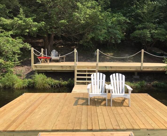 Two white adirondack chairs are sitting on a wooden dock overlooking a body of water.