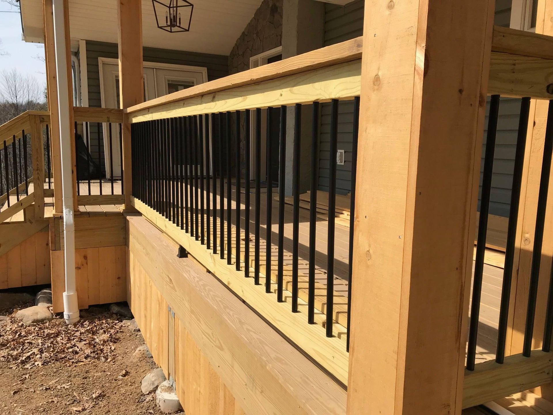A wooden deck with black railing is being built in front of a house.