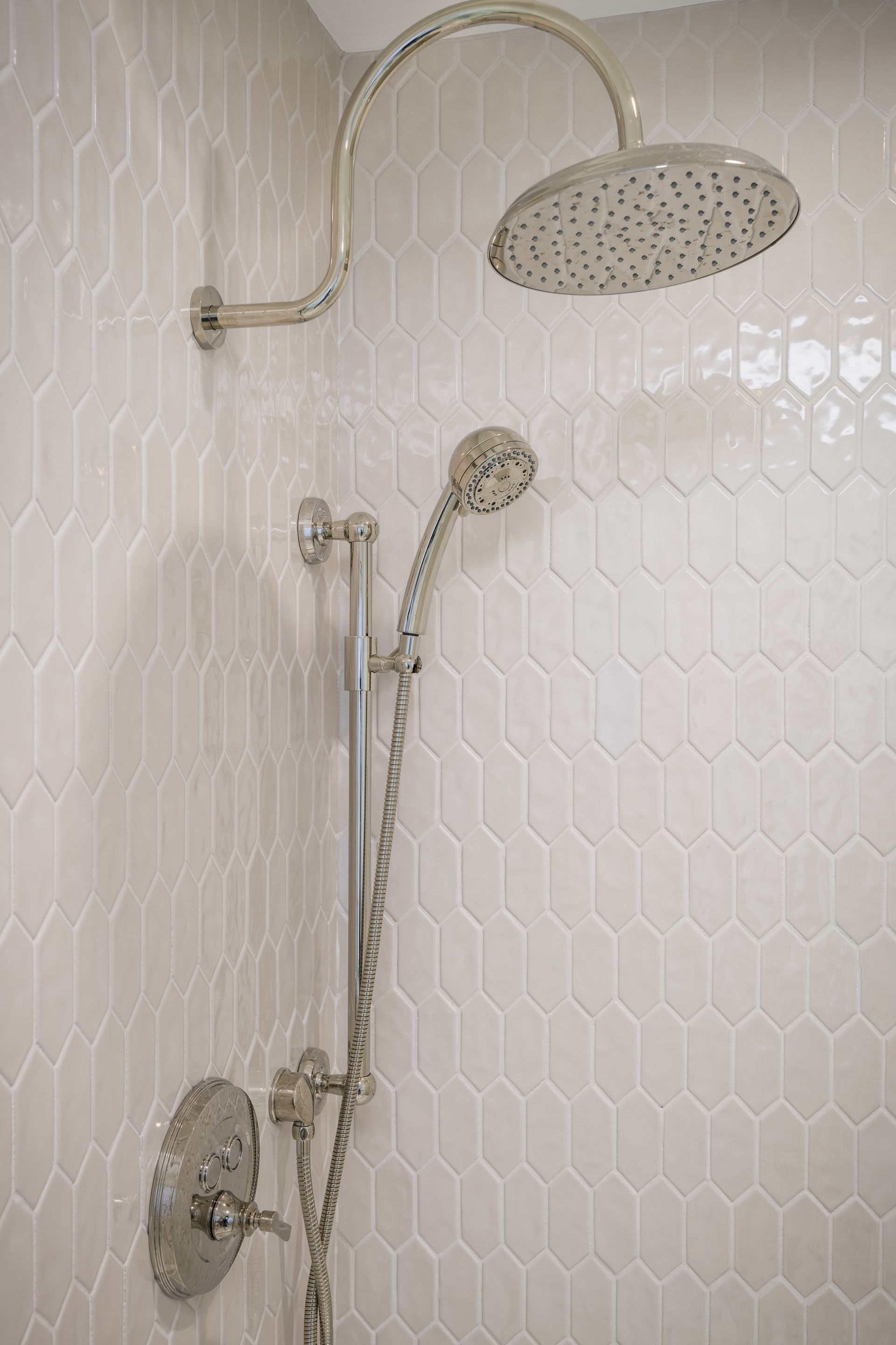 A close up of a shower head in a bathroom with white tiles.