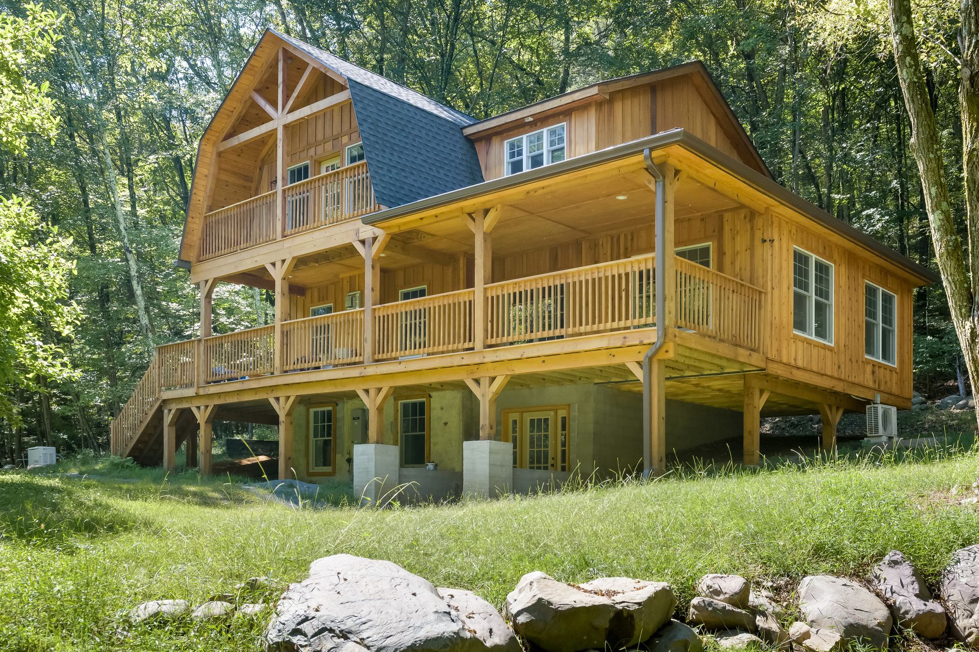 A large wooden house with a large deck is surrounded by trees.