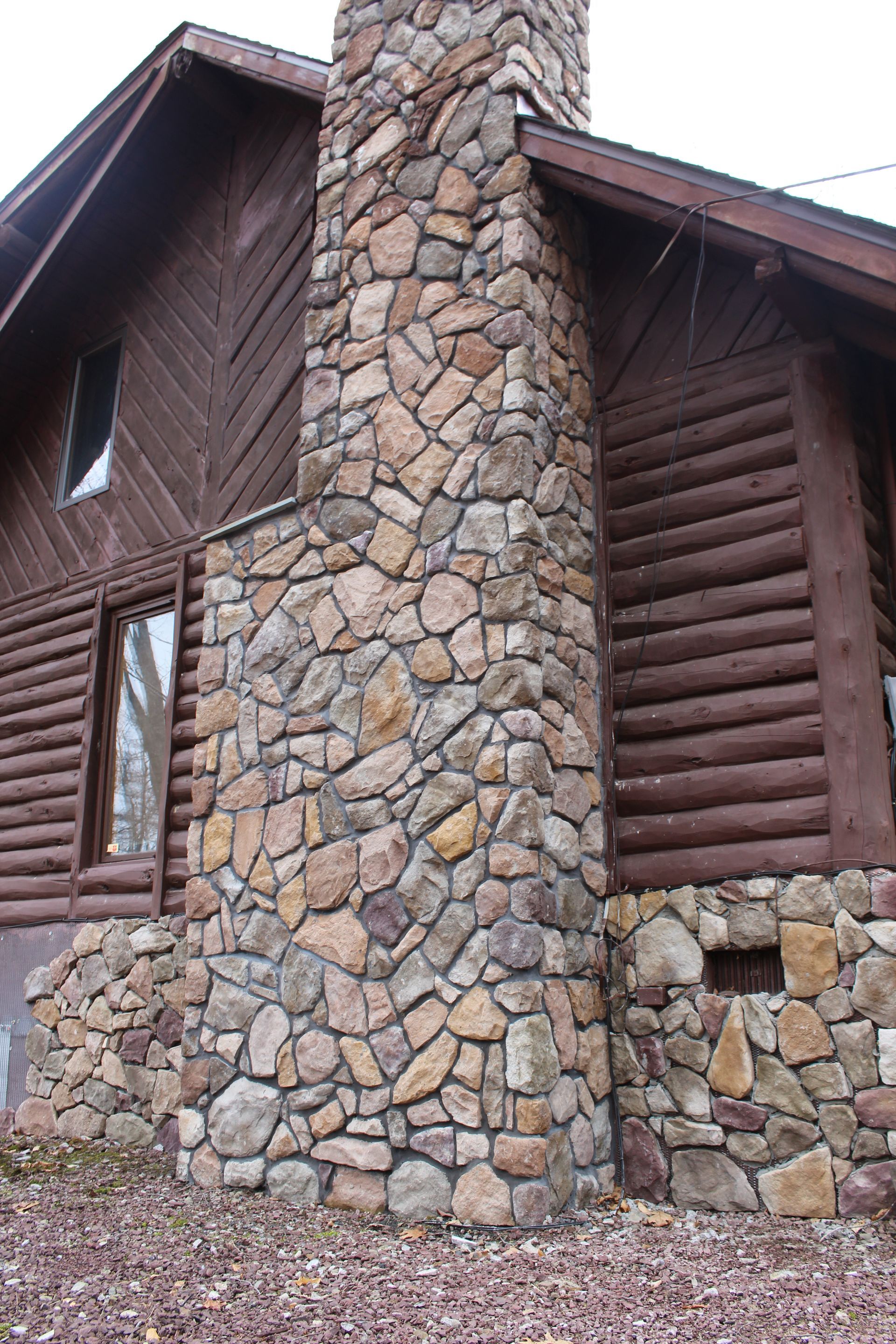 A large stone chimney is on the side of a log cabin.