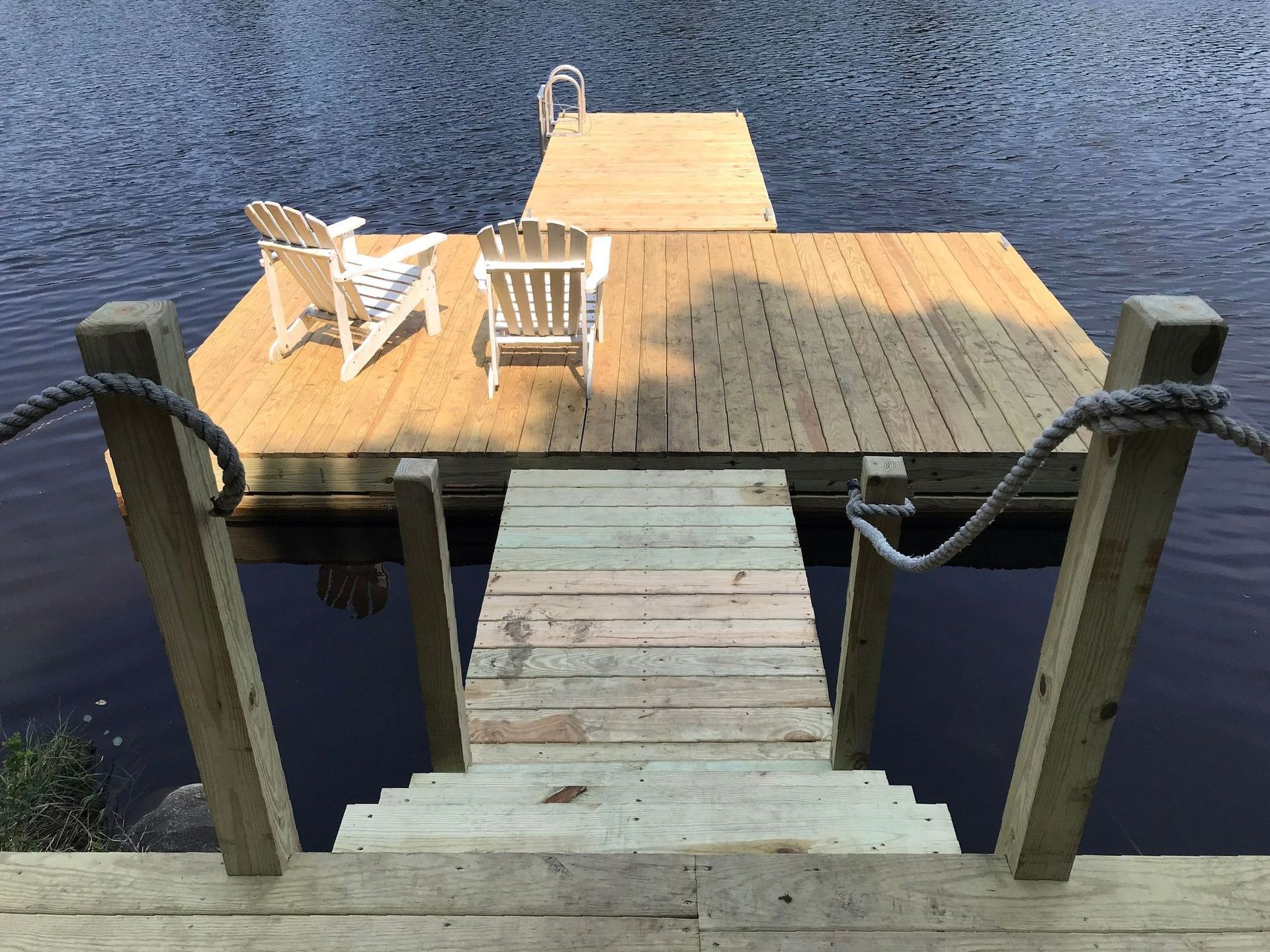 A wooden dock with chairs on it and stairs leading to it.