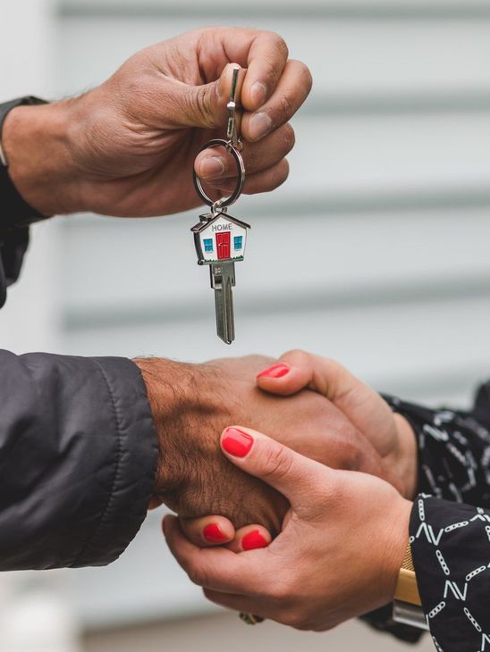 Hands exchanging house keys with a house-shaped keychain during a handshake.