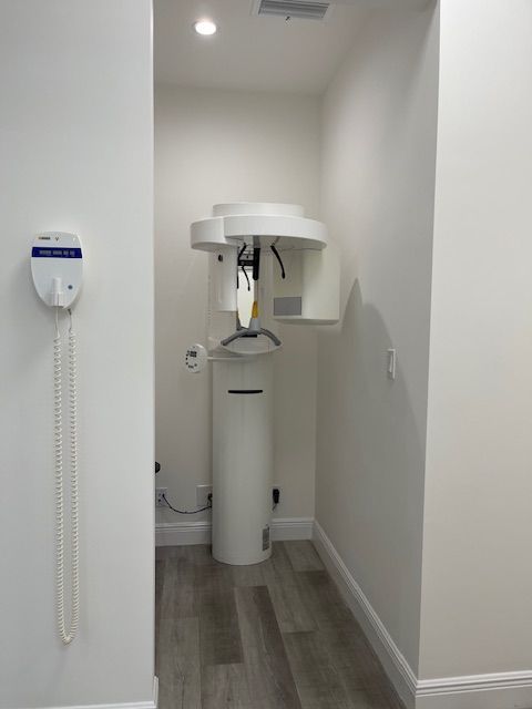 Dental X-ray machine in a narrow white exam room with gray wood-look flooring