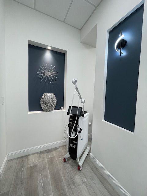 Small white room with wall art and a standing medical device or cart in the corner.