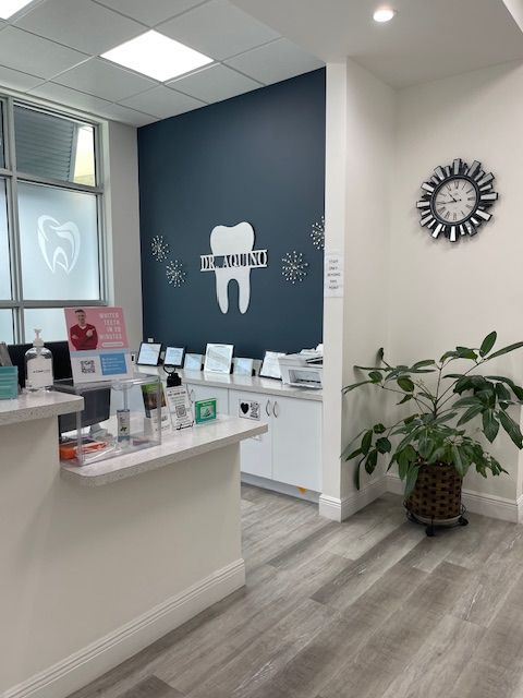 Dental office reception area with white counter, navy accent wall, wall clock, and potted plant