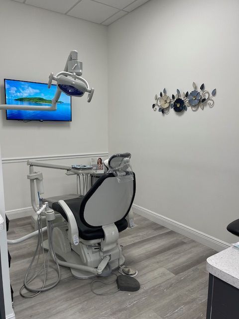 Dental exam room with chair, overhead lamp, monitor, and wall art.