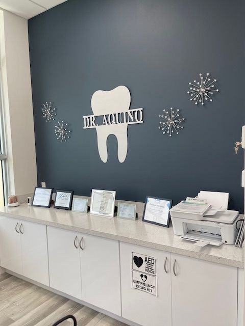 Dental office reception area with dark blue wall, tooth logo, and white cabinets displaying forms.