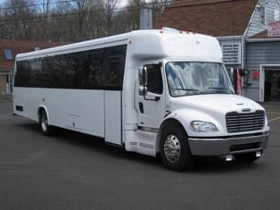 A white Freightliner shuttle bus parked on an asphalt lot in front of a building.