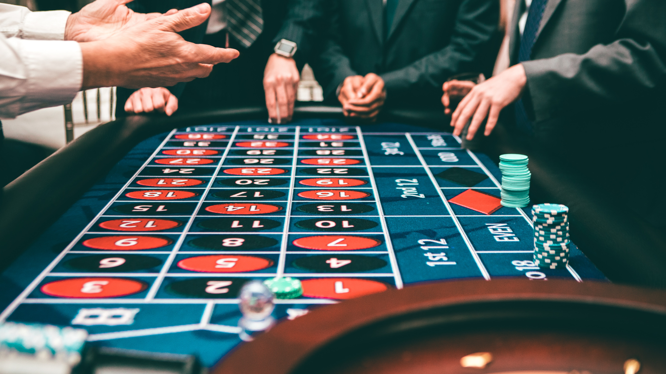 People playing roulette at a gaming table, with hands placing bets on the green felt layout.