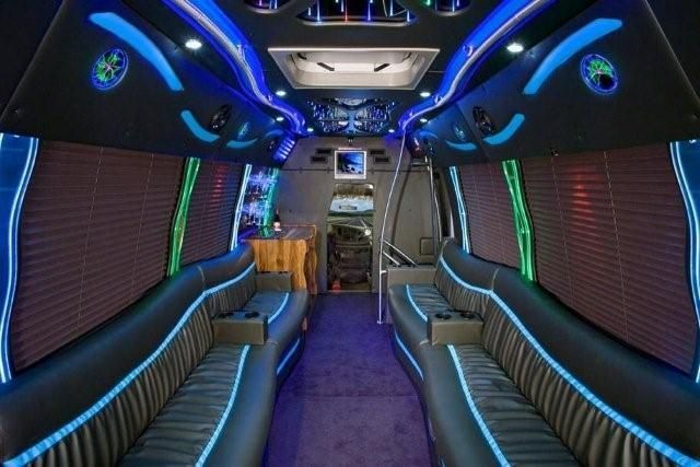Interior of a luxury party bus with plush wrap-around black leather seating, blue LED accent lighting, and wood accents.