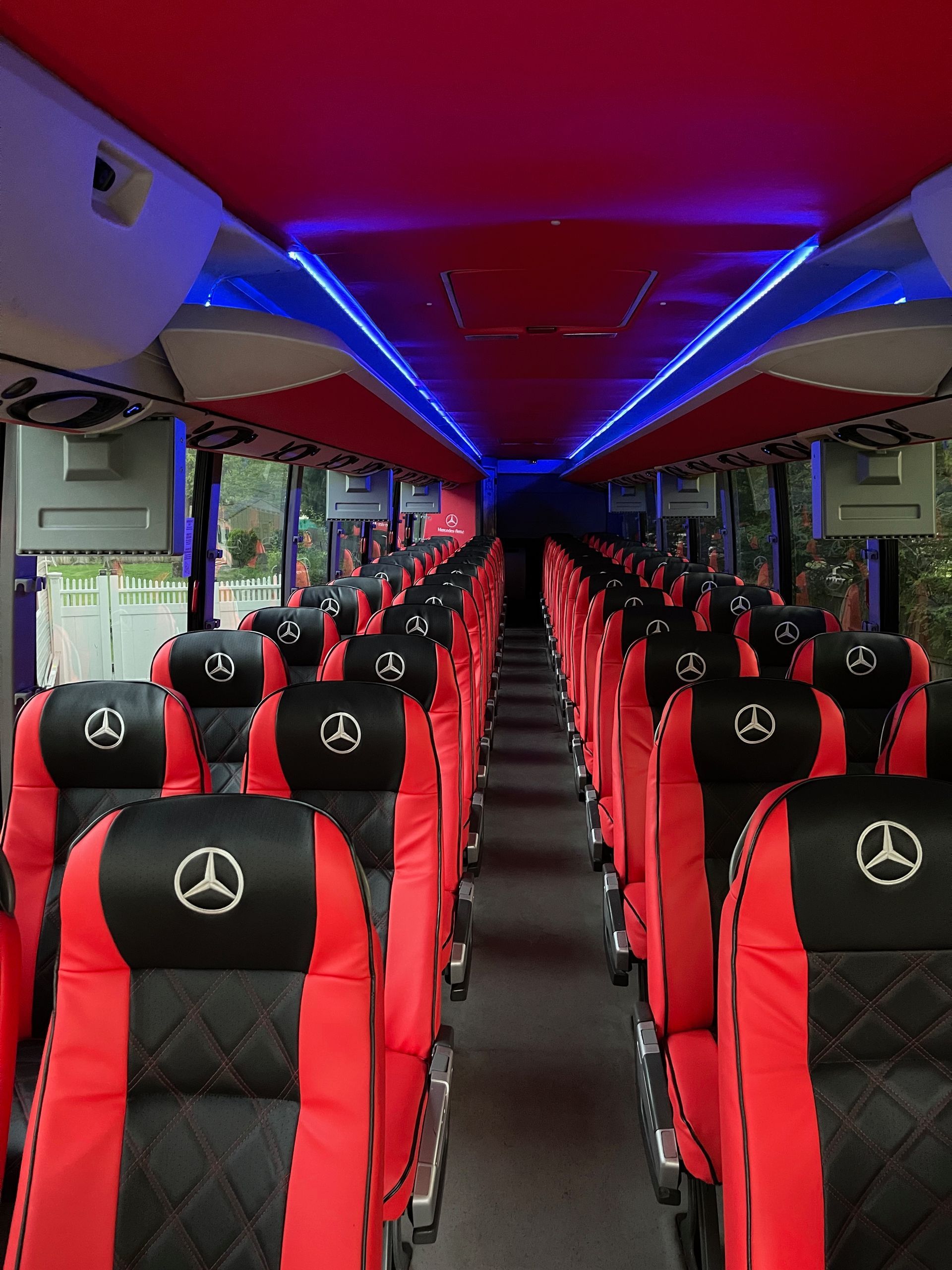 Interior of a bus with red and black patterned seats featuring the Mercedes-Benz logo, illuminated by blue ceiling lights.