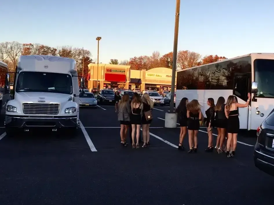 A group of people dressed in black cocktail attire stand in a parking lot between a white shuttle bus and a motorcoach.