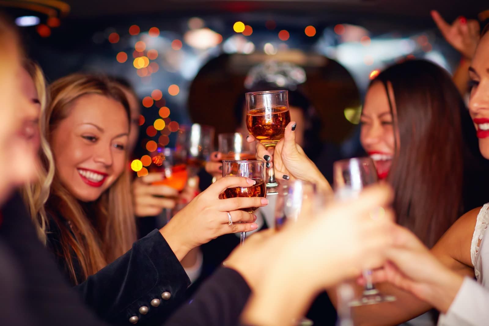 A group of people cheers with glasses of wine in a dimly lit setting with bokeh lights in the background.