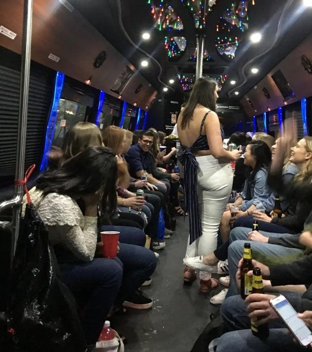 A group of people socializing inside a party bus with blue lighting and overhead decorations.