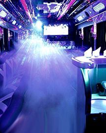The interior of a luxury party bus with vibrant purple ambient lighting, plush seating, and a flat-screen television.