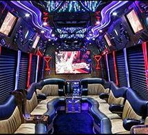 The interior of a luxury party bus with plush two-tone leather bench seating, purple accent lighting, and a large TV.