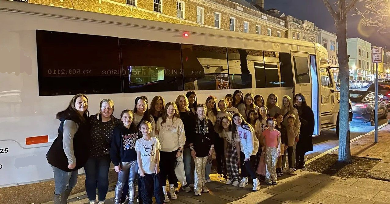 A group of people standing together at night outside a large white party bus parked on a city street.