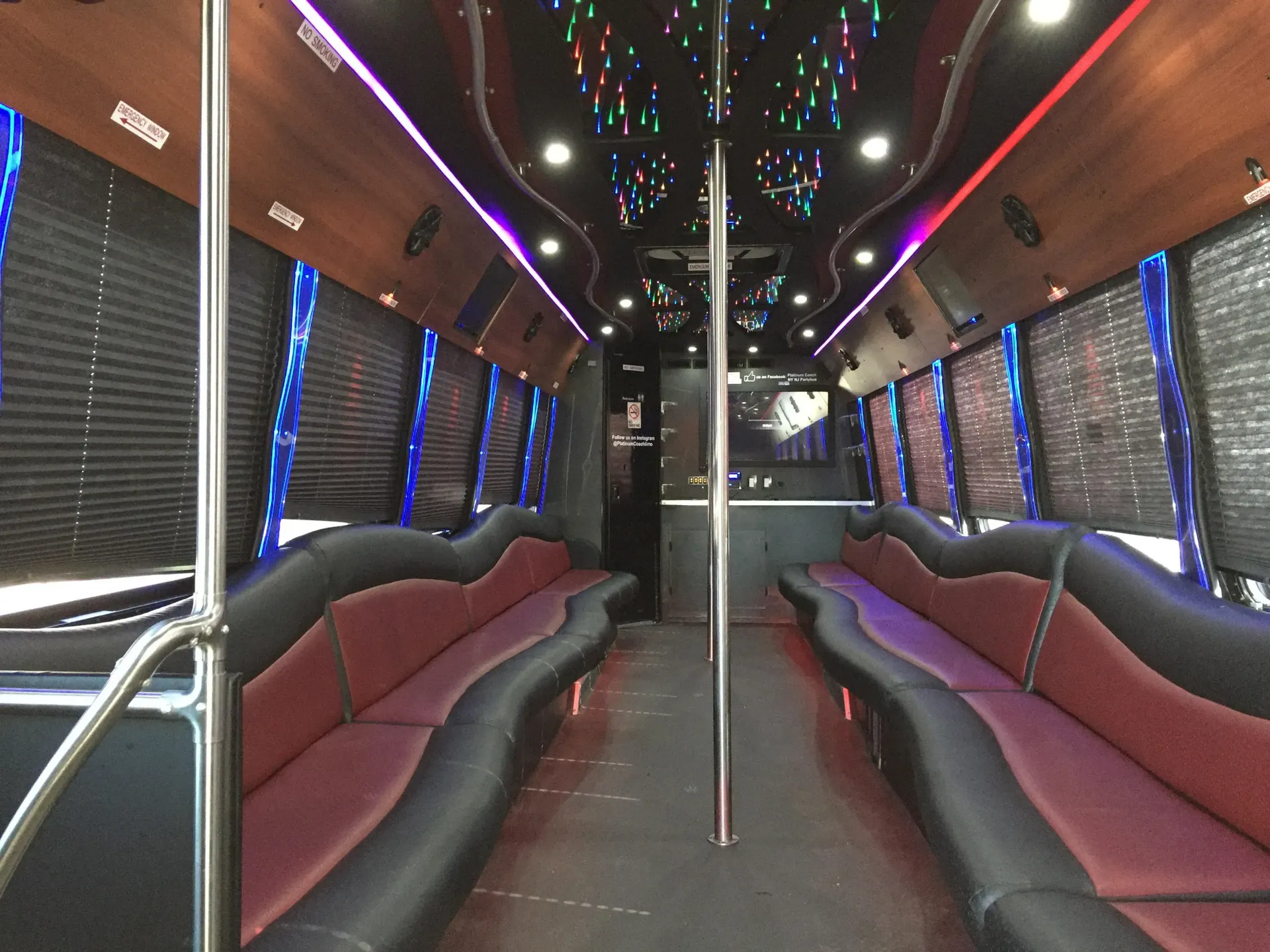 Interior of a party bus featuring wrap-around red and black leather bench seating, a center pole, and colorful ceiling LEDs.