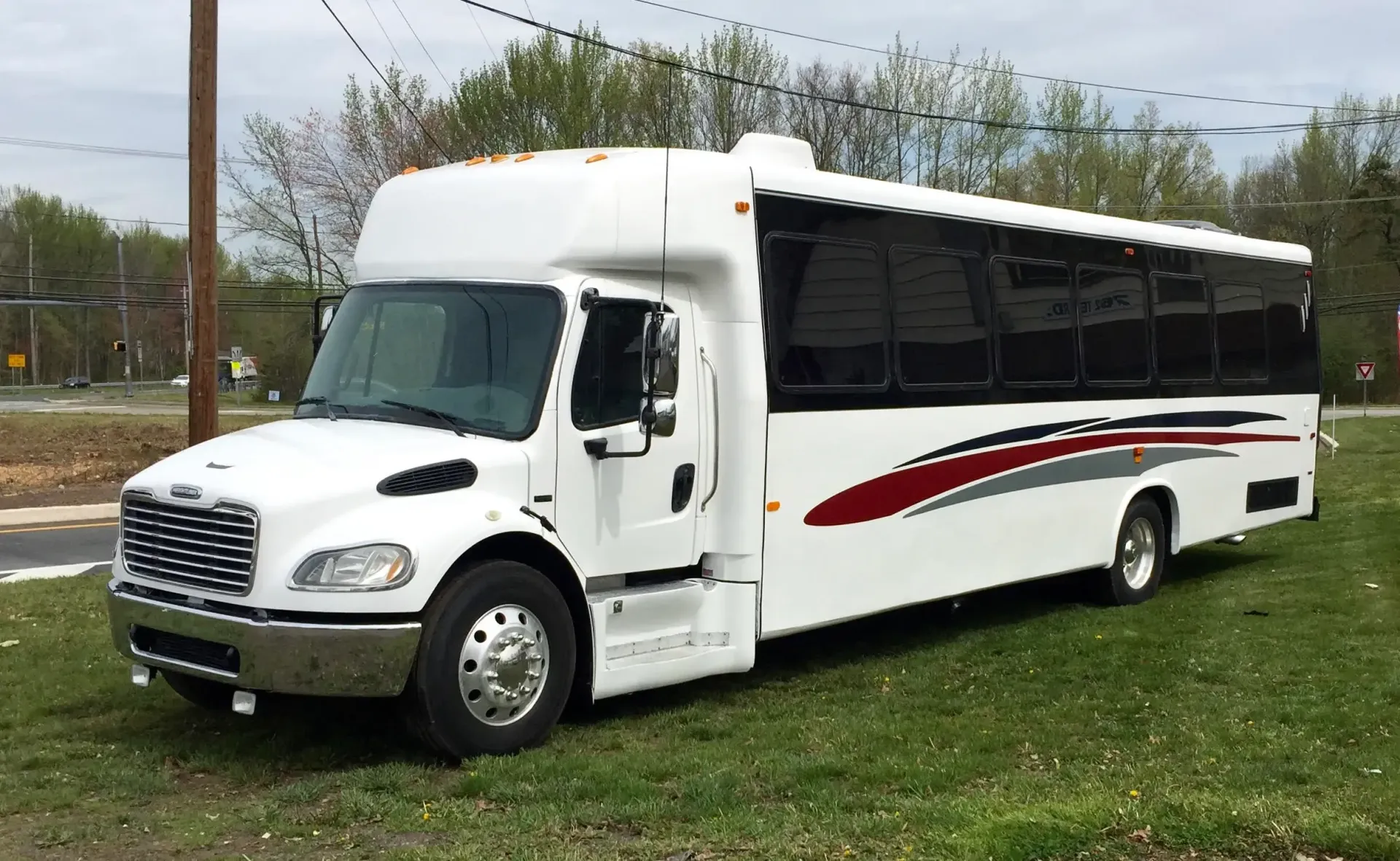 A white shuttle bus with red and grey side decals parked on a grassy area.