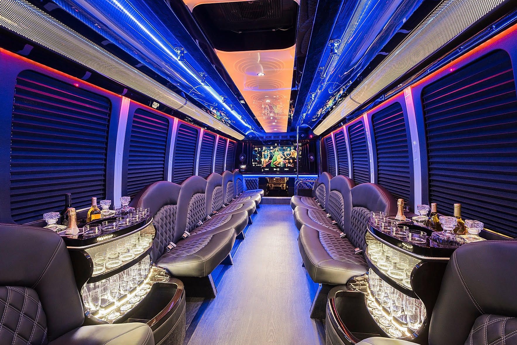 Interior of a luxurious party bus with patterned leather seats, neon blue accent lighting, and mirrored bar areas.
