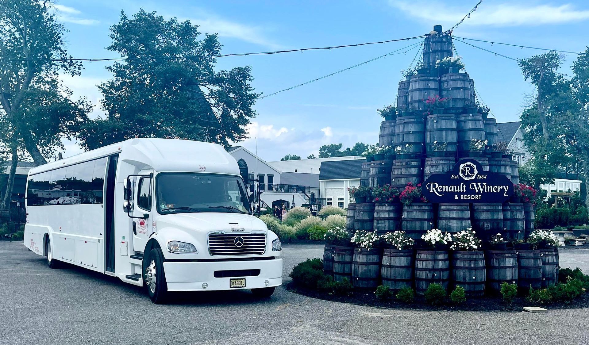 A white minibus parked outdoors next to a tall, decorative pyramid structure built from stacked wooden wine barrels.