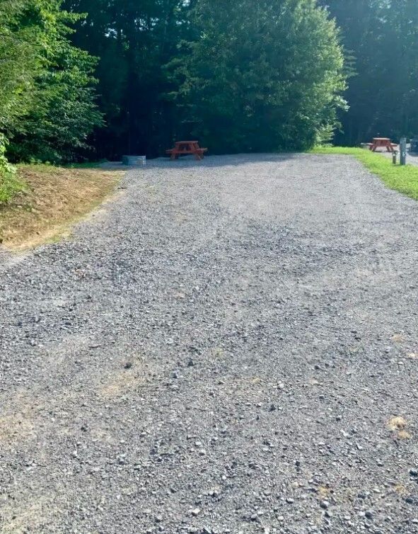 Gravel path leading into a wooded area with picnic tables and a small red sign in the distance