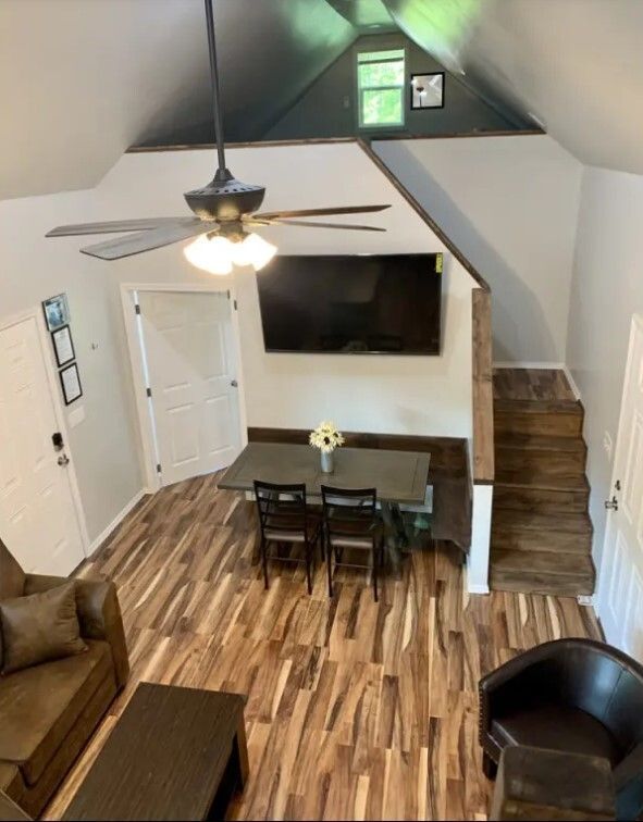 Cozy loft living room with TV, dining table, ceiling fan, stairs, and wood floors.