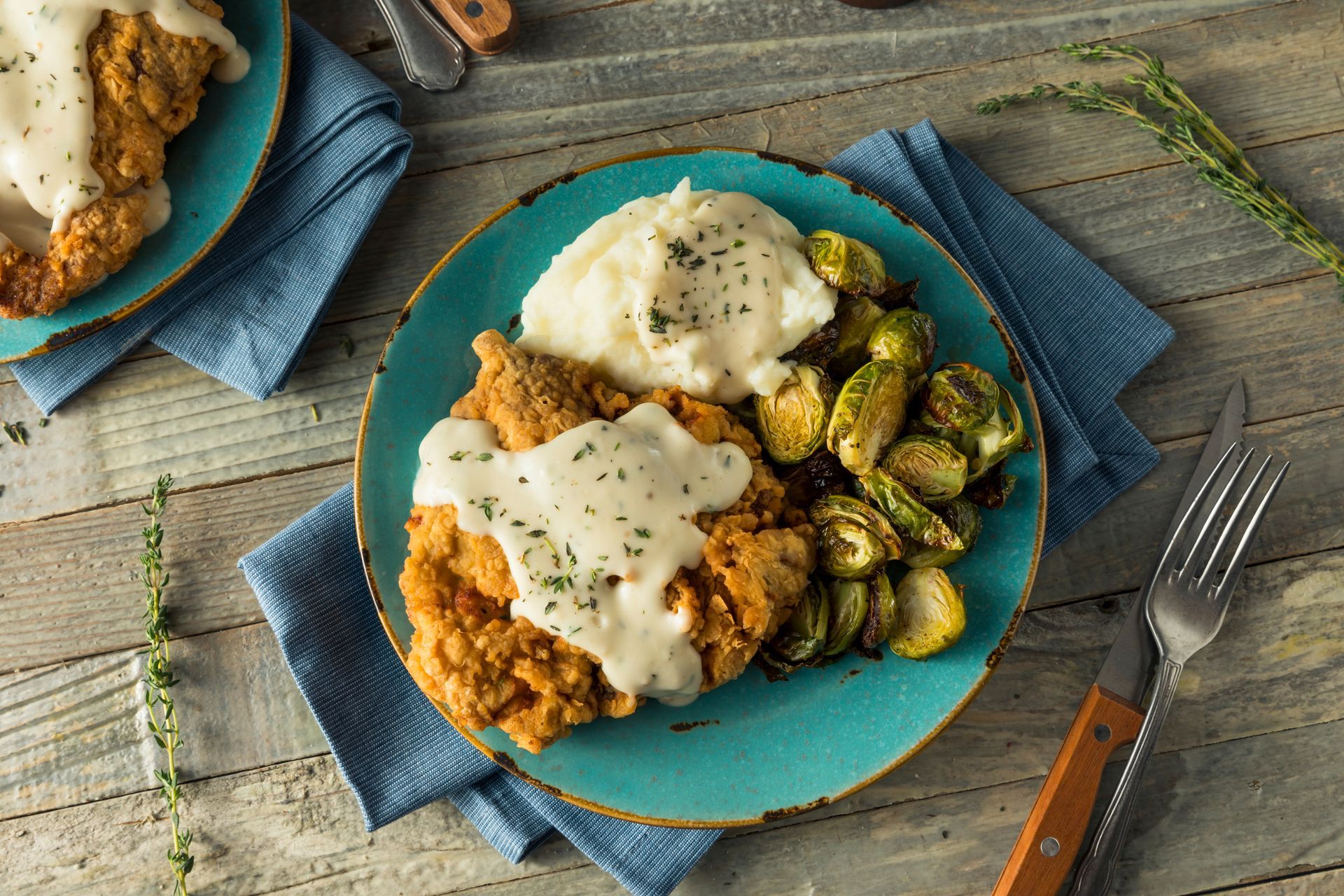 Top-down view of a plated meal with chicken, Brussels sprouts, sauce, and a fork on a rustic table