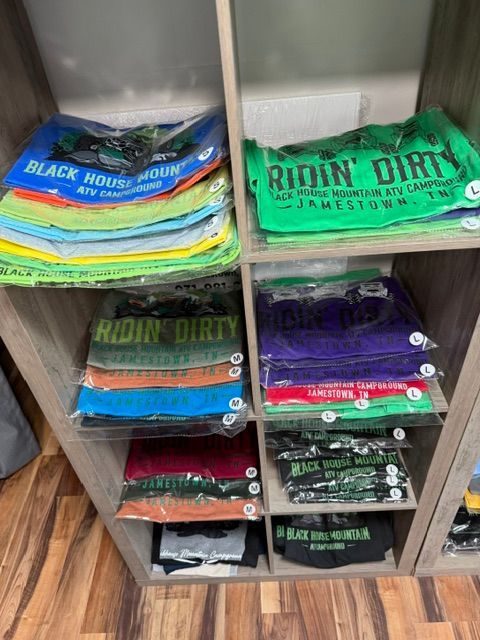 Shelves stacked with folded graphic T-shirts in various colors, including Black Label and Riding Dirty designs