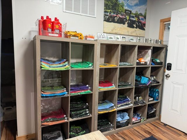 Wooden cubbies filled with folded colorful clothes in a room, with cleaning supplies on top and a white door nearby