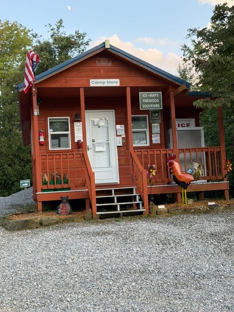 Small red cabin labeled “Garry’s Bar” with an American flag, gravel foreground, and a person sitting on the porch
