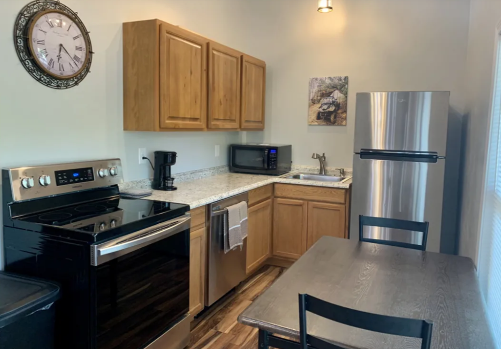 Modern kitchen with black stove, wood cabinets, stainless fridge, and a counter with a chair.